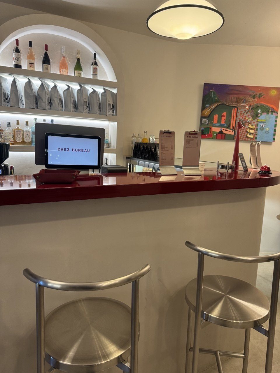 The burgundy counter, the backlit arch of bottles and beans, and a painting on the wall