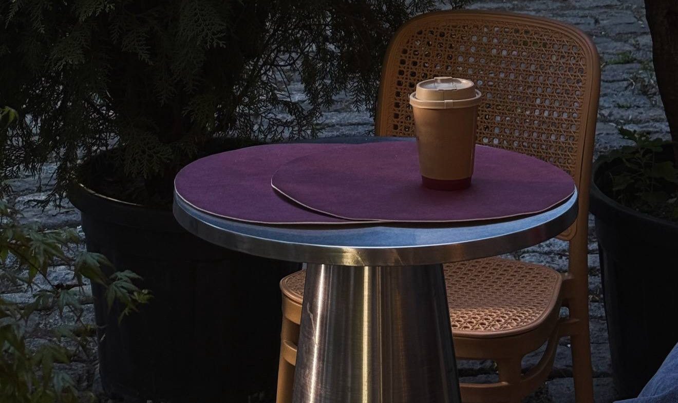 A takeaway cup on a table in the garden, cane chair beside it