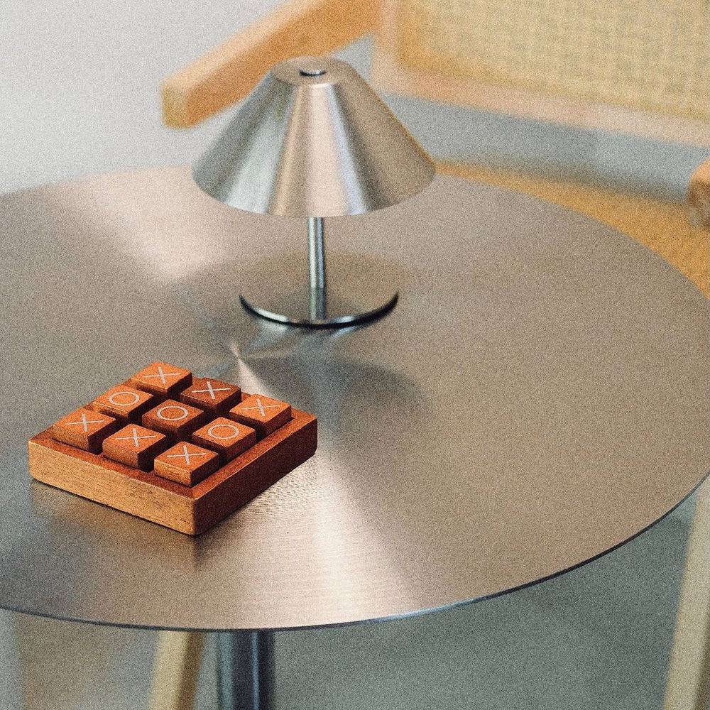 A wooden noughts-and-crosses set and a small lamp on a steel table