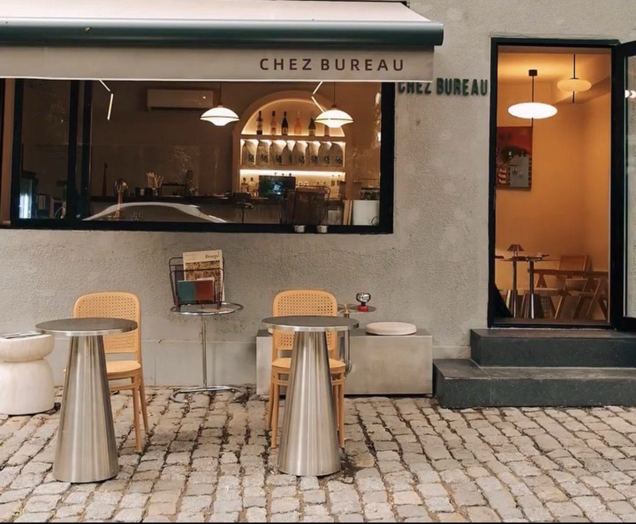 Tables and cane chairs outside the café window by day